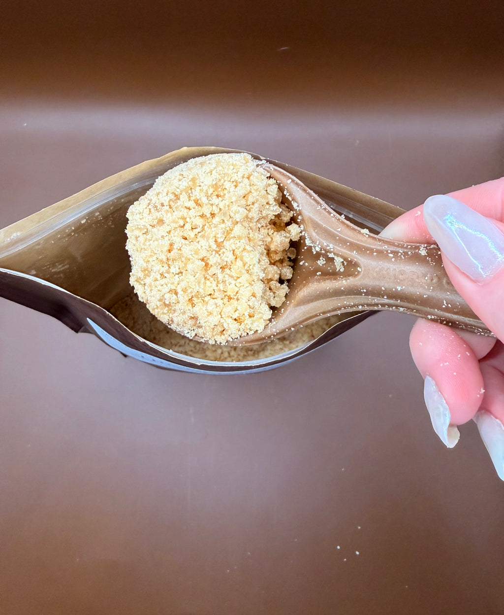 scoop holding laundry scent booster powder over the scent booster pouch, with a brown background