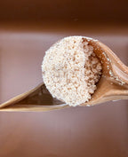 scoop holding laundry scent booster powder over the scent booster pouch, with a brown background