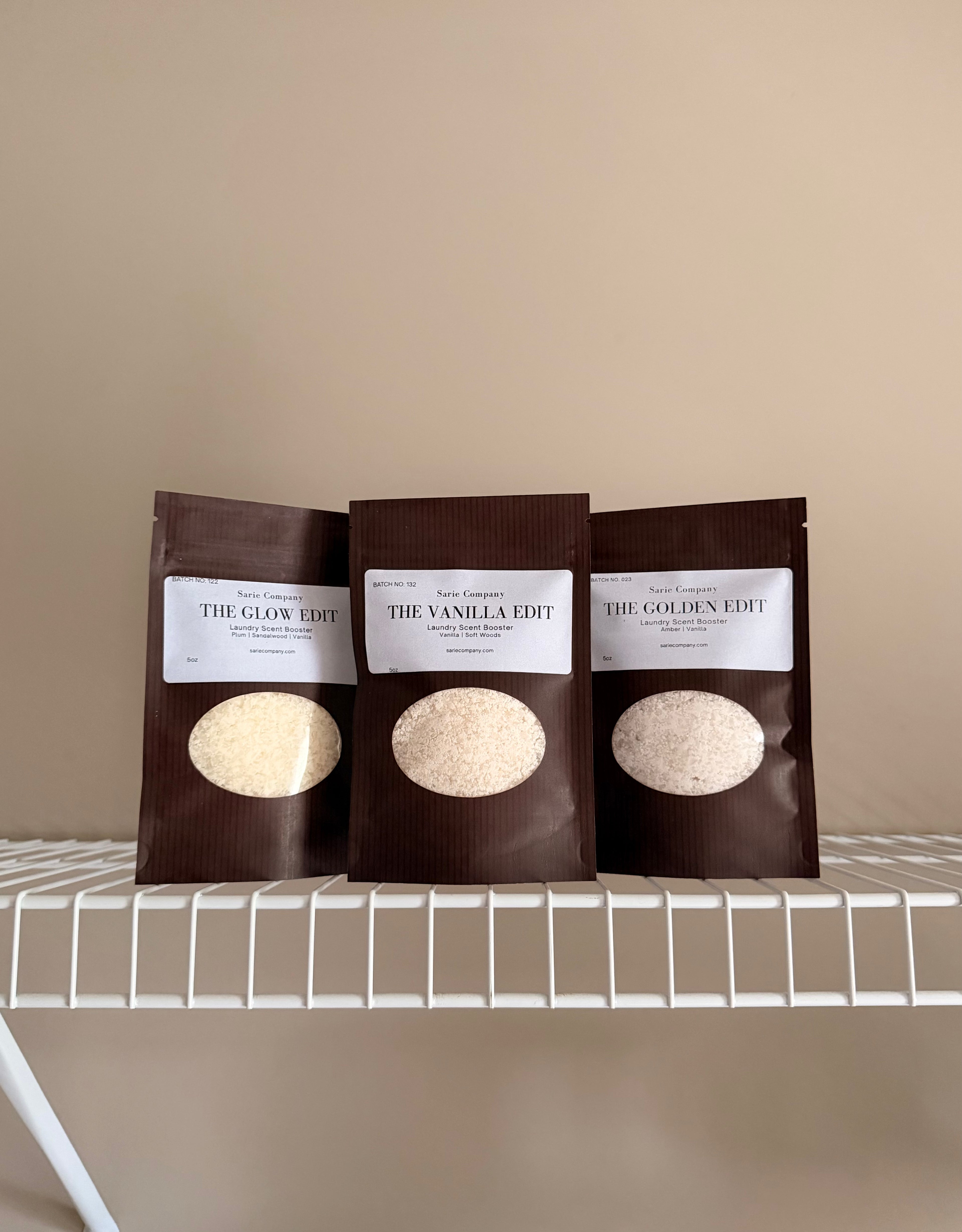 Three laundry scent booster packages in The Vanilla Edit, The Golden Edit, and The glow Edit. On a beige background with a white shelf.