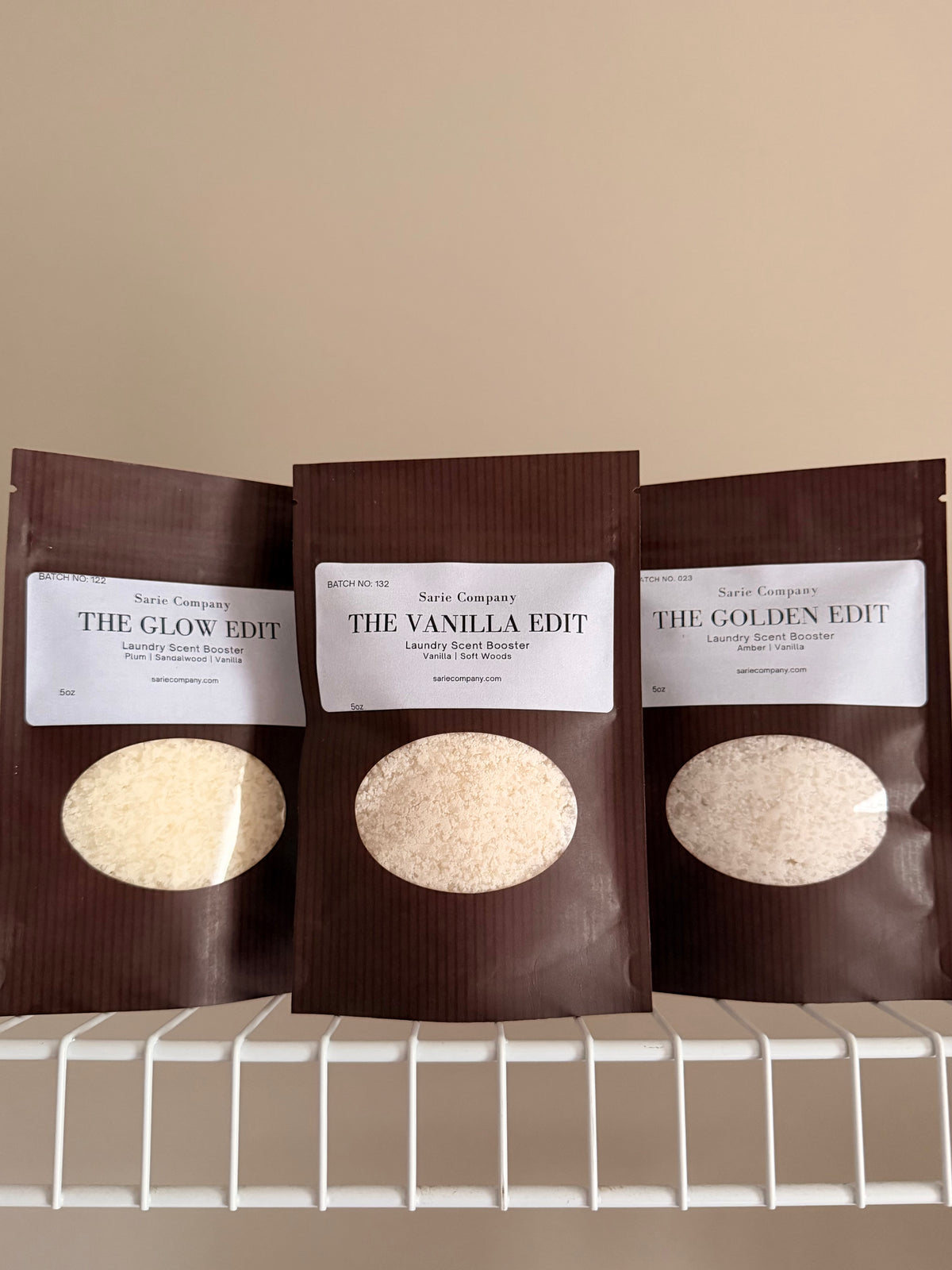 Three laundry scent booster packages in The Vanilla Edit, The Golden Edit, and The glow Edit. On a beige background with a white shelf.