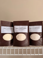 Three laundry scent booster packages in The Vanilla Edit, The Golden Edit, and The glow Edit. On a beige background with a white shelf.