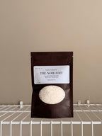 The Noir Edit sampler pouch on a beige background with a white shelf.