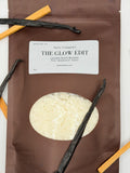 Sarie Company's brown Glow Edit booster package on a white background with vanilla beans and sandalwood pieces.