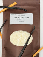 Sarie Company's brown Glow Edit booster package on a white background with vanilla beans and sandalwood pieces.