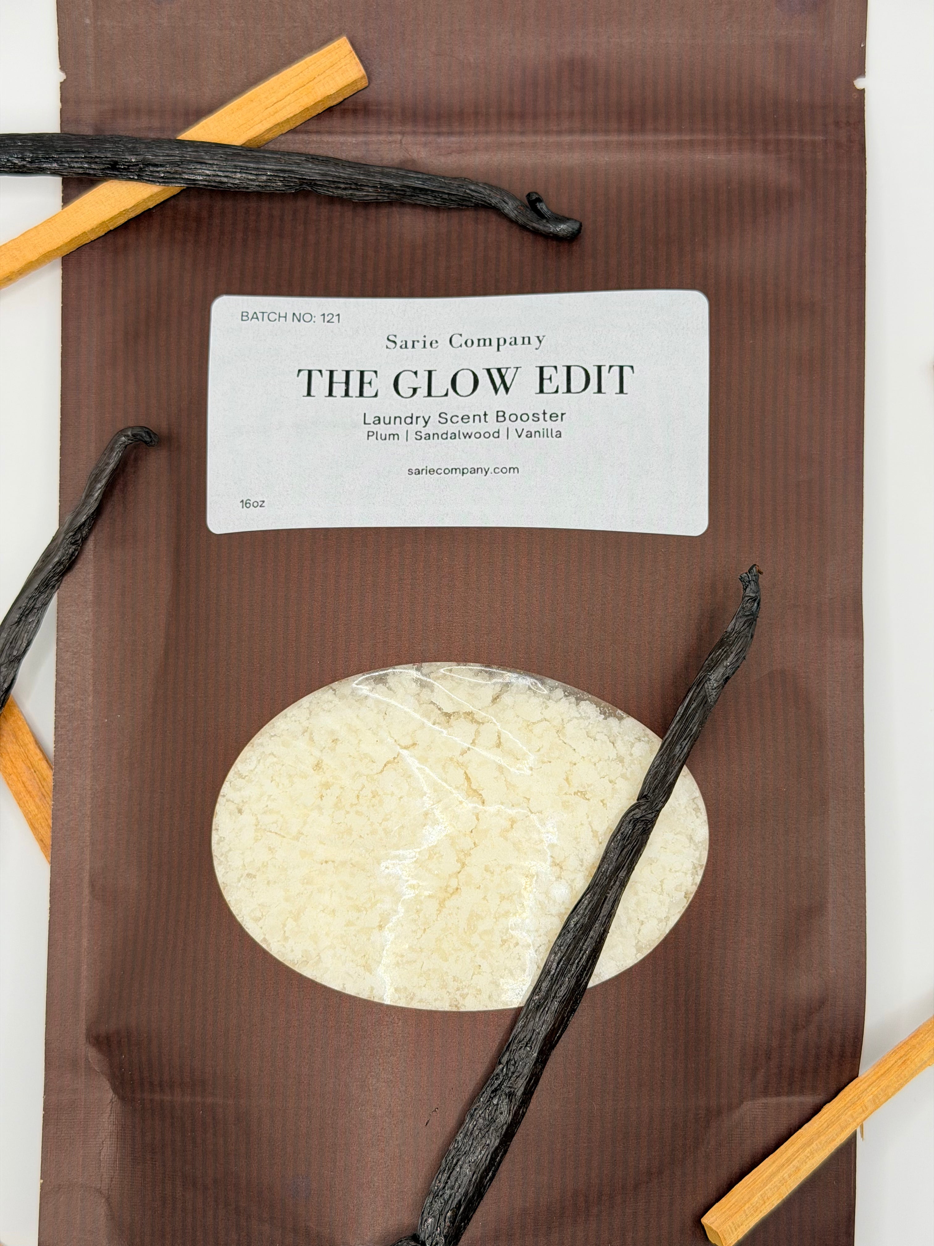 Sarie Company's brown Glow Edit booster package on a white background with vanilla beans and sandalwood pieces.