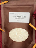 Sarie Company laundry scent booster package with a label on a red fabric background with pieces of sandalwood.